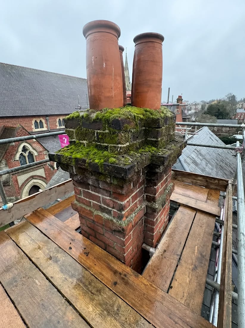 Old moss-covered chimney stack with three terracotta pots before repair work