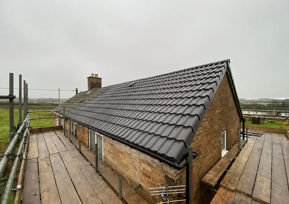 Completed dark grey tiled roof on a bungalow with black guttering and scaffold